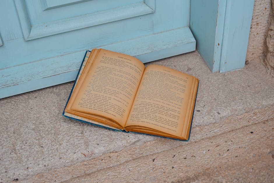 An open vintage book resting on stone steps by a light blue door.