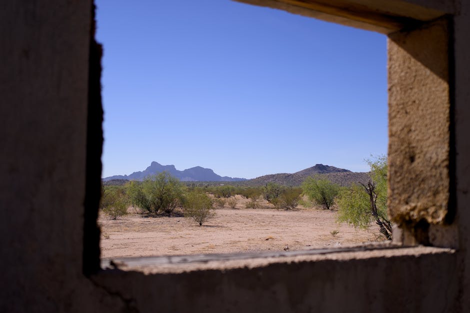 A scenic view of desert terrain with mountains through a window frame of a ruined structure.
